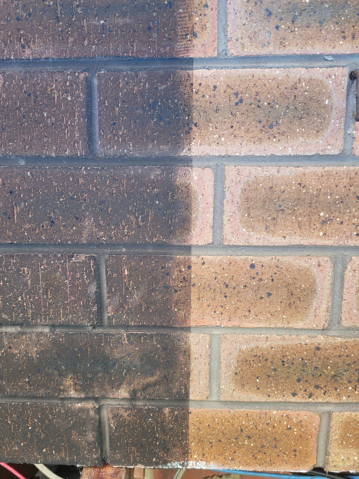 Brick wall with half cleaned and half soot-covered surface showing fire damage restoration progress